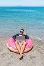 Businessman using laptop computer on inflatable donut on tropical beach. Summer vacation concept Royalty Free Stock Photo