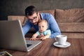 Businessman using a laptop computer for work at home while looking after his baby son. Royalty Free Stock Photo