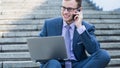 Businessman using laptop pc and mobile phone. He is sitting on a stairs. Royalty Free Stock Photo