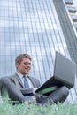 Businessman using laptop, sitting on the grass near the office building Royalty Free Stock Photo
