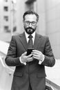 Businessman using mobile app texting outside of office in urban city with skyscrapers buildings in background. Caucasian bearded Royalty Free Stock Photo