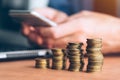 Businessman using smartphone with stacked coins in foreground