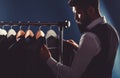 Businessman in vest, row of suits in shop. Stylish man in a cloth jacket. It is in the showroom, trying on clothes