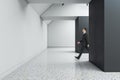 Businessman walking in creative concrete exhibition hall interior with daylight, mock up place. Royalty Free Stock Photo