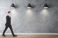 Businessman walking in gallery interior with three ceiling lamps Royalty Free Stock Photo