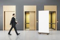 Businessman walking in grey concrete interior with three elevator doors and empty mockup poster. Royalty Free Stock Photo