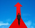 Businessman walking on growing red arrow in sky Royalty Free Stock Photo