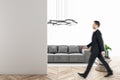 Businessman walking in modern bright white living room interior with empty mock up place on wall, couch, table, wooden flooring Royalty Free Stock Photo