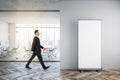 Businessman walking in modern glass office interior with empty mock up banner on wall, wooden flooring, furniture, window with Royalty Free Stock Photo