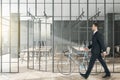 Businessman walking in modern glass partition and bike in stylish coworking office interior with city view Royalty Free Stock Photo