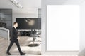 Businessman walking in modern meeting room interior with empty mockup poster, large table, wooden flooring, equipment, glass