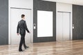 Businessman walking in modern office lobby interior with steel elevators, empty white poster, wooden flooring and tile wall. Mock Royalty Free Stock Photo