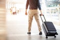 Businessman walking outside public transport building with luggage in rush hour. Business traveler pulling suitcase in modern airp