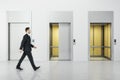 Businessman walking in white concrete interior with three elevator doors. Royalty Free Stock Photo