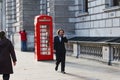 Businessman walks past old red phone booth in london while talking on mobile phone