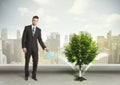 Businessman watering green tree on city background