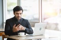 Businessman wear black suit using smartphone working laptop sitting in coffee shop. Royalty Free Stock Photo