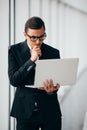 Businessman wearing glasses and suit working laptop holding hands near panoramic window. Royalty Free Stock Photo