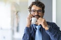 Businessman wearing glasses, talking on the phone while holding a cup of coffee and looking at the camera Royalty Free Stock Photo