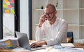 Businessman wearing glasses talking on phone, sitting at desk with laptop at office Royalty Free Stock Photo