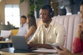 Businessman Wearing Wireless Headphones Working On Laptop In Informal Seating Area Of Modern Office Royalty Free Stock Photo