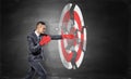 A businessman wears boxing gloves and breaks a chalk drawing of a round archery target.