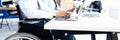 Businessman in wheelchair with colleague in office at working table