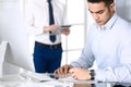 Businessman working with computer in modern office, male colleague at background . Headshot of arab male entrepreneur or