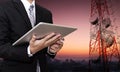 Businessman working on digital tablet, with satellite dish telecom network on telecommunication tower at countryside city in