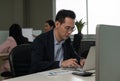 Businessman working on laptop computer sitting at office desk in her workstation with colleagues in background Royalty Free Stock Photo