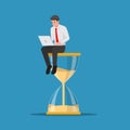 Businessman working with laptop sitting on big hourglass Royalty Free Stock Photo