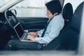 Businessman working in laptop and talking on the phone in the drivers seat in his car