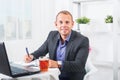 Businessman working in office, sitting at table with a laptop, looking smiling. Royalty Free Stock Photo