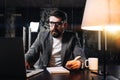 Businessman working process at open space office at night. Bearded coworker using modern laptop and sits by the wooden table with Royalty Free Stock Photo