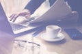 Businessman working at sunny office on laptop while sitting at the wooden table.Man holding paper documents in hands Royalty Free Stock Photo