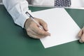 Businessman writes on a sheet of white paper. Wood background. Dressed in a shirt and tie. Close-up Royalty Free Stock Photo