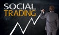 Businessman writes social trading on blackboard concept