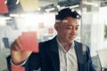 Businessman writing on sticky notes on glass wall while working in modern office Royalty Free Stock Photo