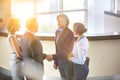 Businessmen greeting while standing with colleagues at reception lobby in office