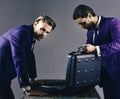 Businessmen look into opened briefcase on dark background.