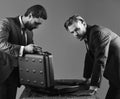 Businessmen look into opened briefcase on dark background.