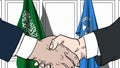 Businessmen or politicians shake hands against flags of Saudi Arabia and United Nations. Official meeting or cooperation