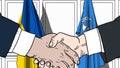 Businessmen or politicians shake hands against flags of Ukraine and United Nations. Official meeting or cooperation