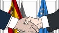 Businessmen or politicians shake hands against flags of Spain and United Nations. Official meeting or cooperation