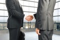 Businessmen shake hands in empty loft style room with glassy win