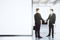 Businessmen shake hands in loft office with blank white wall, mo
