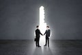 Businessmen shaking hands in concrete interior with abstract bright keyhole opening. Success, teamwork, future and leadership
