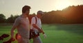 Businessmen walking golf course outside. Two players carry clubs in sportswear.