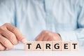 Businessmen wear a white shirt at their desks in the office. Use your hand to pick up a wooden cube inscribed with the word Target