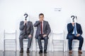 Businesspeople sitting in queue and waiting for interview, holding question marks in office Royalty Free Stock Photo